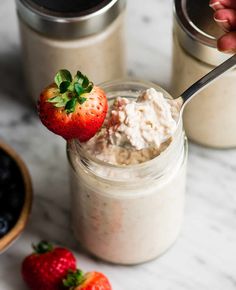 a person is holding a spoon with some oatmeal and strawberries on it