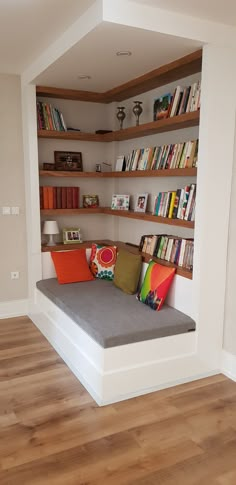 a room with some bookshelves and a couch in the corner that has pillows on it