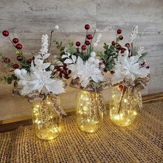 three vases with flowers and lights are sitting on a table