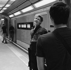 two people standing in front of a train at a station with one person on the platform