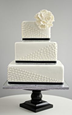 a three tiered white wedding cake with pearls and a flower on top