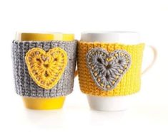 two crocheted coffee mugs with hearts on them, one is yellow and the other is gray