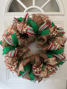 a christmas wreath with green and red bows on the front door, hanging from a white door