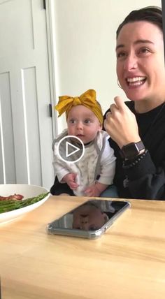 a woman holding a baby in her lap while sitting at a table with food on it