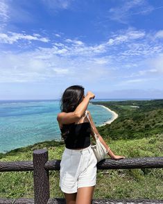 a woman standing on top of a lush green hillside next to the ocean looking at the sky