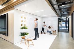 three people standing in front of a whiteboard with plants on it and writing on the wall