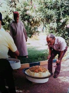 a group of men standing around a table with food on it and one man bending over