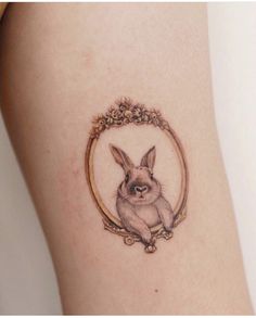 a small rabbit tattoo on the side of a woman's thigh, with an oval frame around it