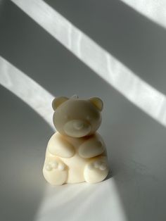 a small white teddy bear sitting on top of a table next to a shadow from the window