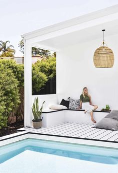 a woman sitting on a bench next to a swimming pool in a house with white walls