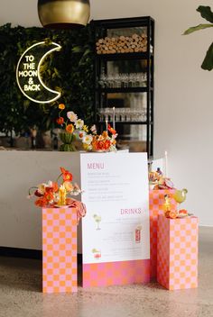 there is a menu on the table next to two boxes with flowers in them and a lite up sign