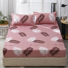 a bed covered in pink and white sheets with palm leaves on the coverlet, next to a window