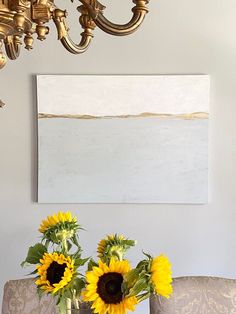 two sunflowers sit on a table in front of a painting and chandelier