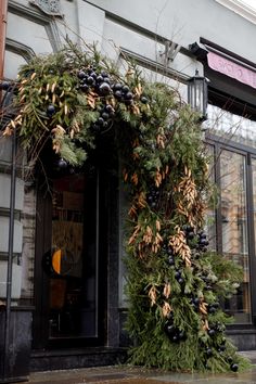 an outdoor christmas wreath on the side of a building with evergreens and berries hanging from it