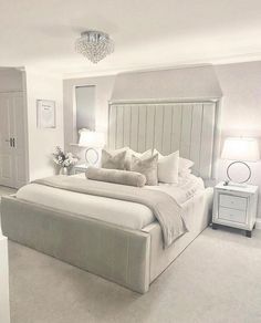 a large white bed sitting inside of a bedroom next to a dresser and lamps on either side of the bed