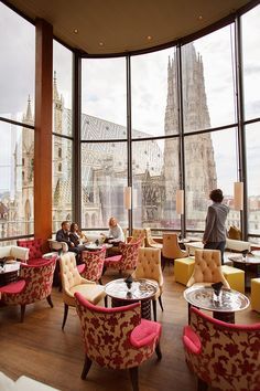 people are sitting at tables in a restaurant with large windows looking out onto the city