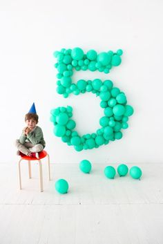 a young boy standing on top of a stool in front of a number 5 balloon wall