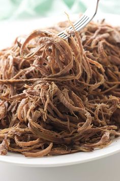 a white bowl filled with shredded meat and a fork stuck in the top of it