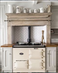 an old fashioned stove in the middle of a kitchen with cups on top of it