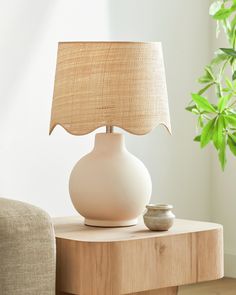 a white lamp sitting on top of a wooden table next to a potted plant