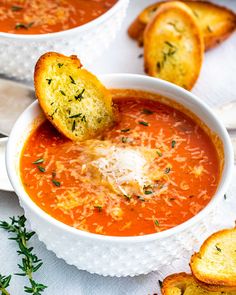 a bowl of tomato soup with bread on the side and parmesan croutons in the background