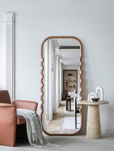 a mirror sitting on top of a white wall next to a chair and table in a room