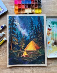 an art project with watercolors and paints on the table next to it is a painting of a tent in the woods