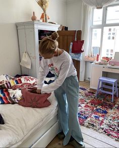 a woman in white shirt and blue pants standing over a bed with pillows on it