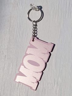 a pink keychain with the word now on it hanging from a metal hook