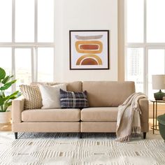 a living room scene with focus on the couch and pillows in front of large windows