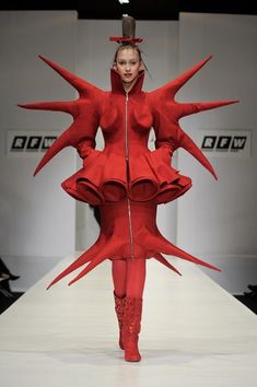 a woman is walking down the runway wearing red clothes and boots with spikes on her head