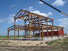 a large wooden structure sitting on top of a dirt field next to a red barn