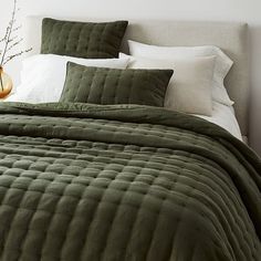 a bed with green bedspread and pillows on top of it next to a vase