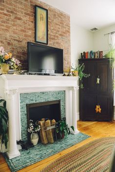 a living room with a fireplace, television and potted plants on the mantel