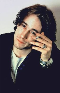 a man with long hair holding his hand to his face and looking at the camera