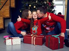 a man and woman kissing while sitting on the floor next to presents under a christmas tree