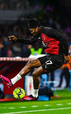 a man kicking a soccer ball on top of a field with people in the background