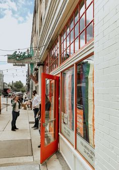 people are standing on the sidewalk in front of a store with red doors and windows