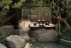 a small pond surrounded by large rocks in a garden with an outdoor dining table and chairs