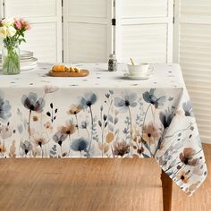 a table covered with a white and blue flowered tablecloth next to a vase filled with flowers