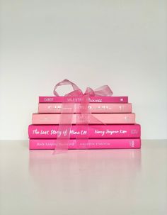 three pink books stacked on top of each other with a ribbon tied around the book ends