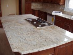 a kitchen with an island in the middle and marble counter tops on both sides, along with wooden cabinets