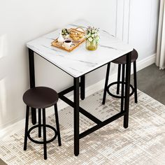 two stools and a table with food on it in front of a white wall