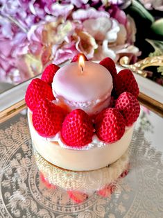 a small white cake with strawberries on top and a lit candle in the middle