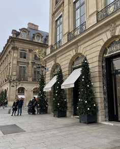 people are walking around in front of a building with christmas trees on the sidewalk and awnings