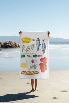 a person standing on the beach holding up a towel with pictures of fish and vegetables