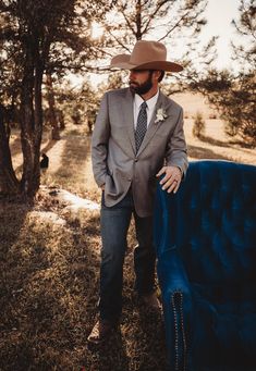 a man in a suit and tie standing next to a blue chair with a cowboy hat on