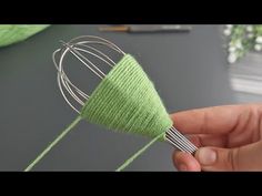 a hand holding a wire whisk with green yarn