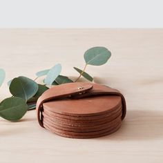 a stack of brown leather coasters sitting on top of a wooden table next to green leaves