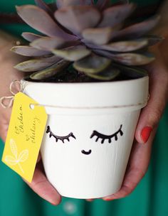 a woman holding a potted plant with eyelashes on it's face and a yellow tag